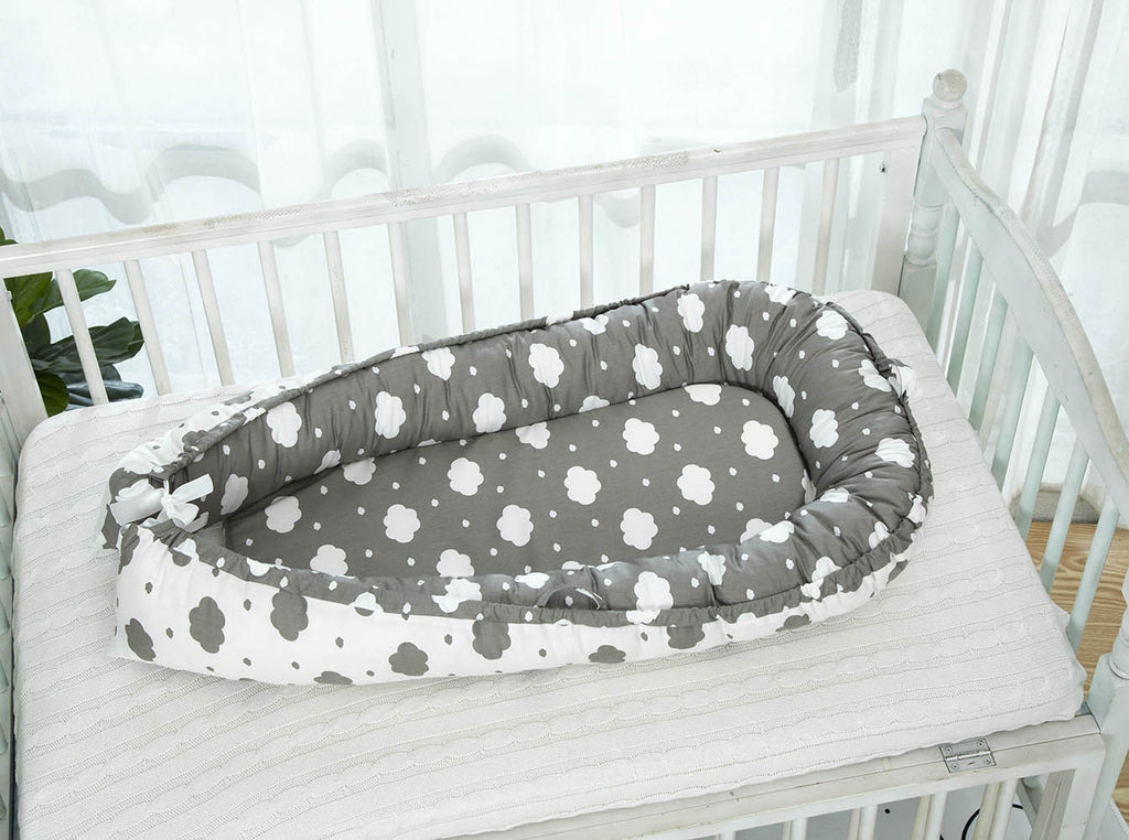 Grey portable baby crib with white clouds in a cot